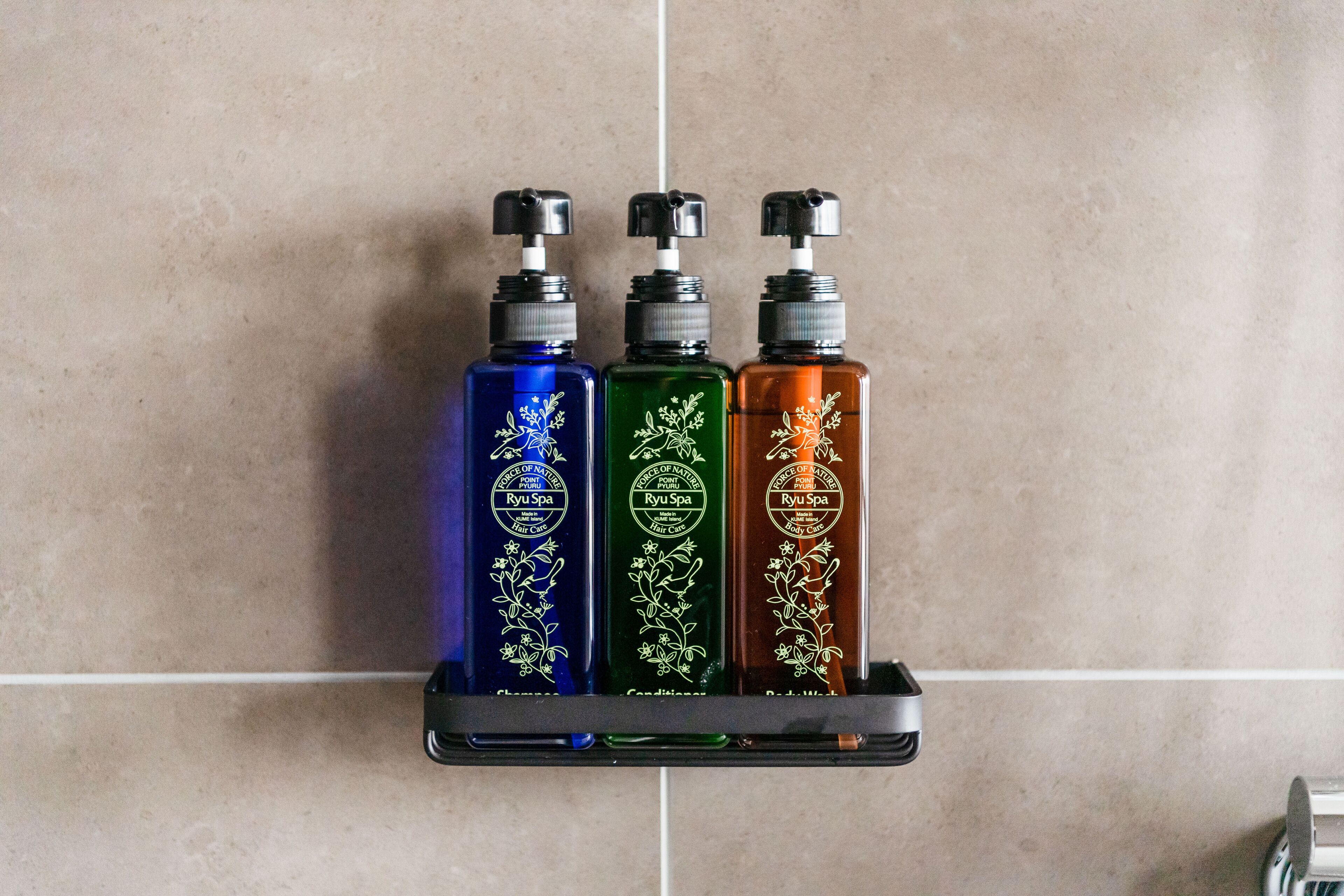 Three bottles of Ryu Spa body wash on a black shelf against a tiled wall.