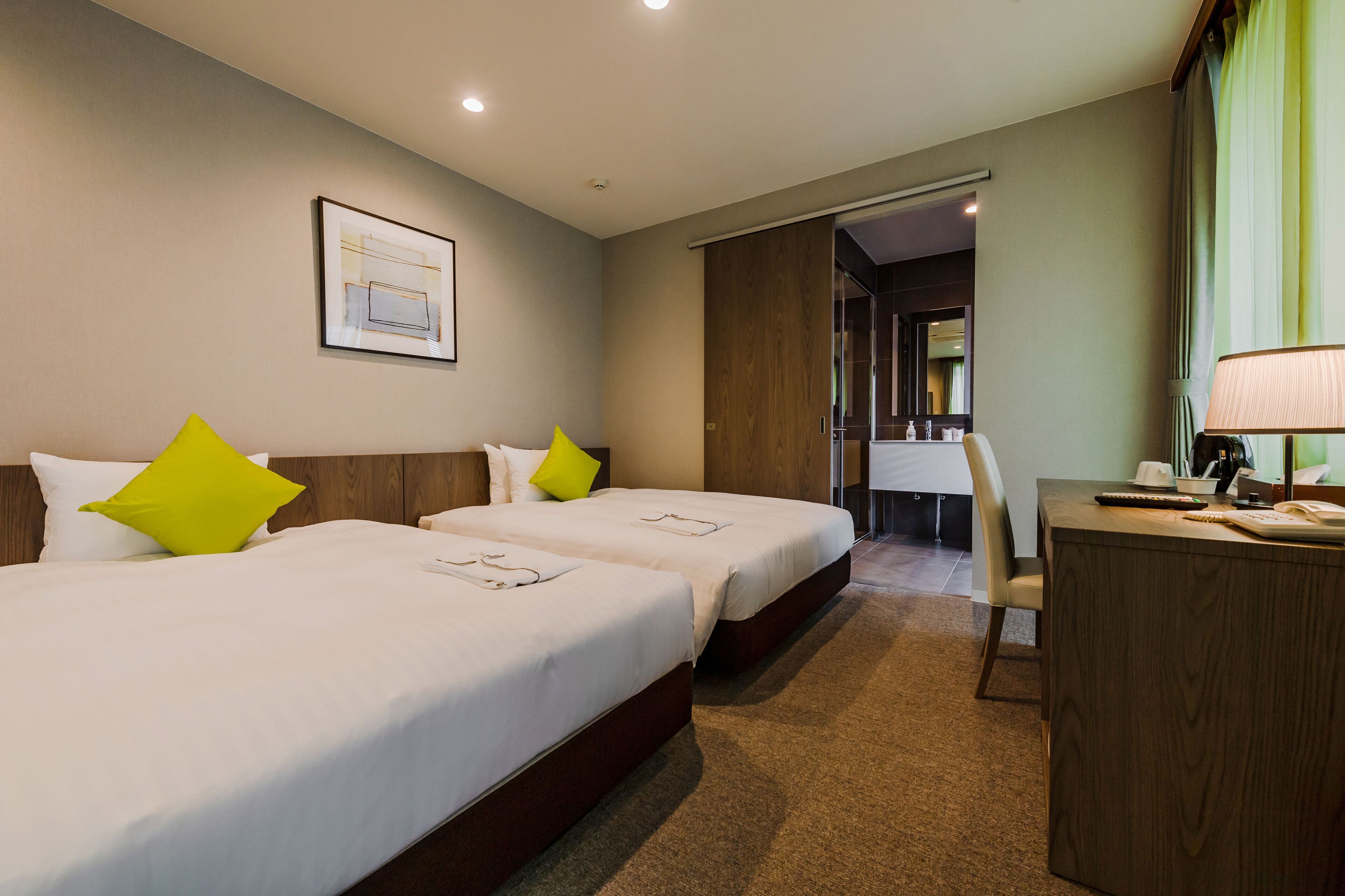 A hotel room with two beds, a desk, and a bathroom visible through an open door.