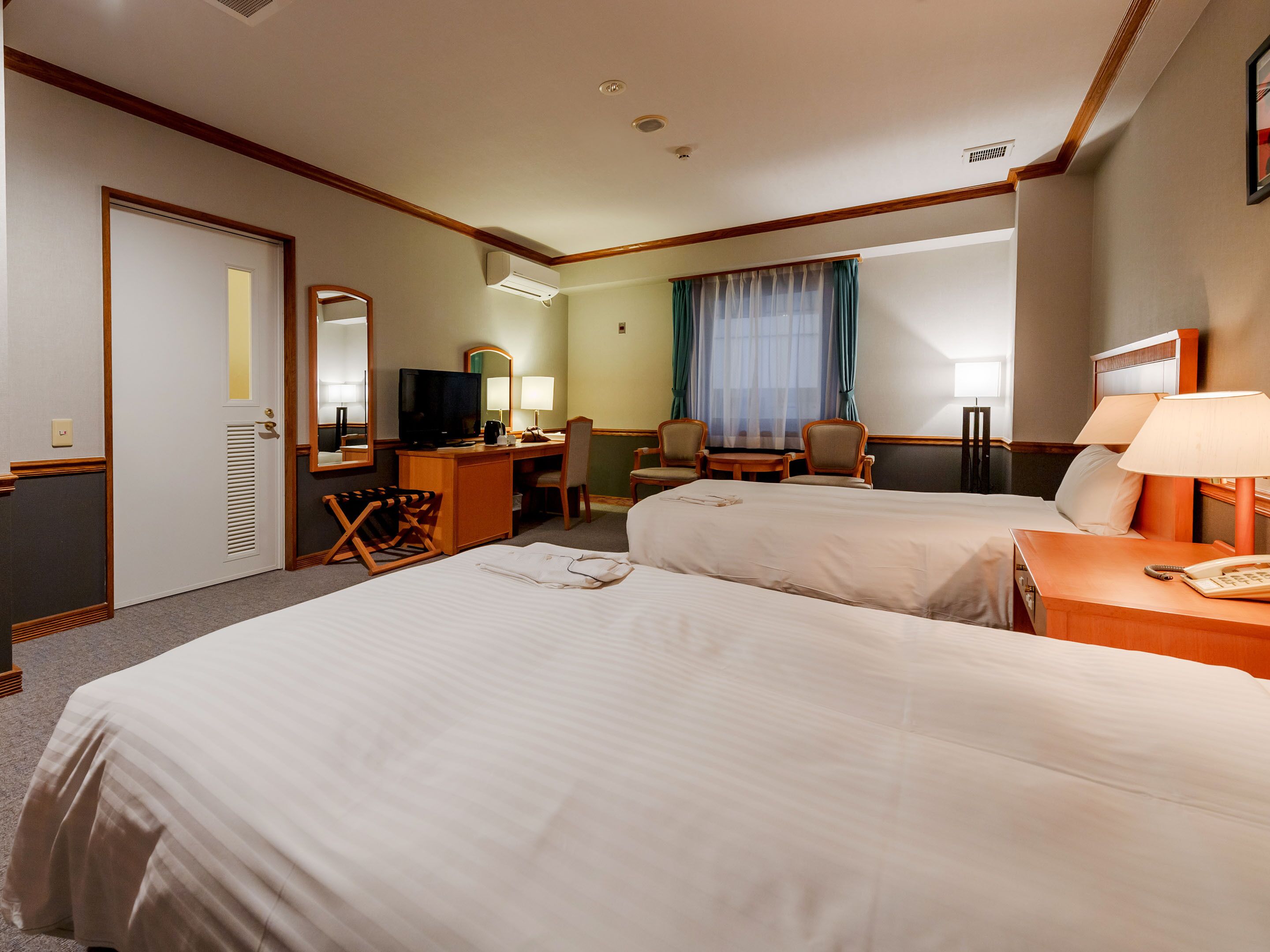 A hotel room with two beds, a desk with a television, a chair, and a desk lamp.