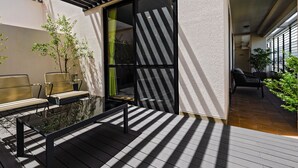 A modern outdoor seating area with a glass table and chairs, surrounded by potted plants and a wooden deck. - HOTEL AZAT Naha (Naha)