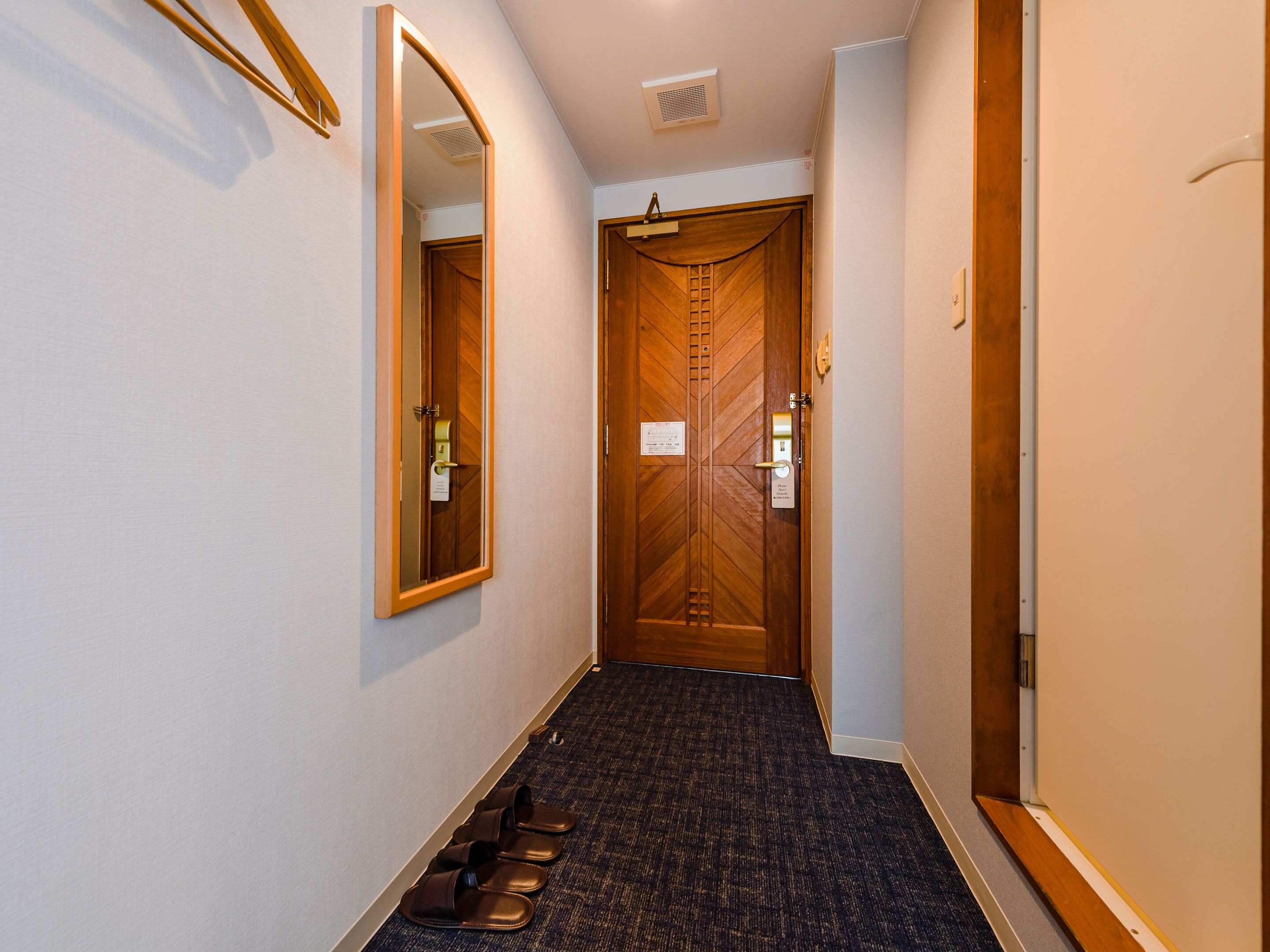 A hallway with a wooden door, a mirror, and a pair of shoes on the floor.