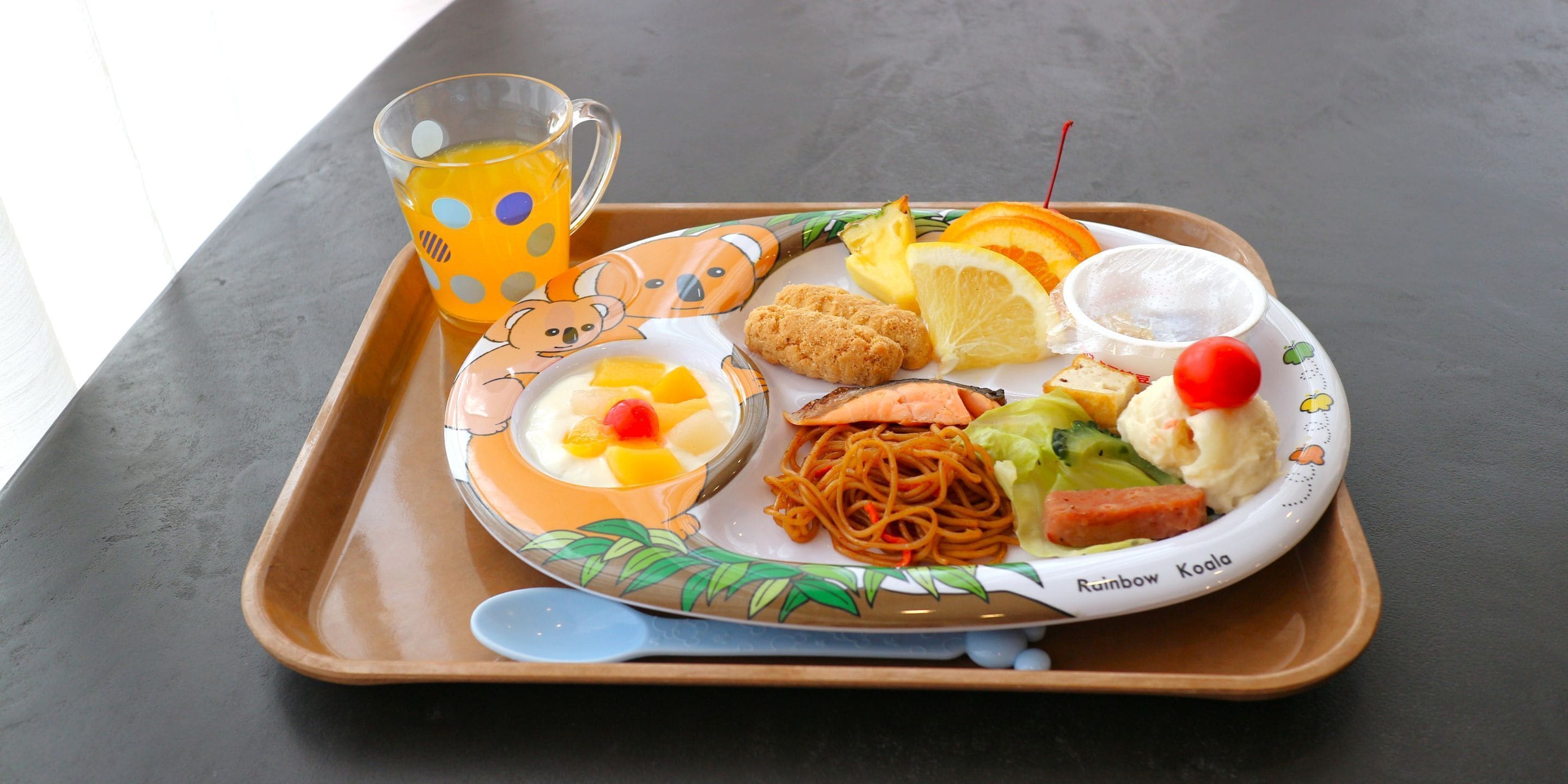 A tray with a variety of food items including noodles, vegetables, and a dessert, along with a glass of juice.