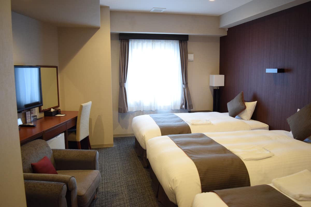 A hotel room with two beds, a desk with a chair, a television, and a window with curtains.