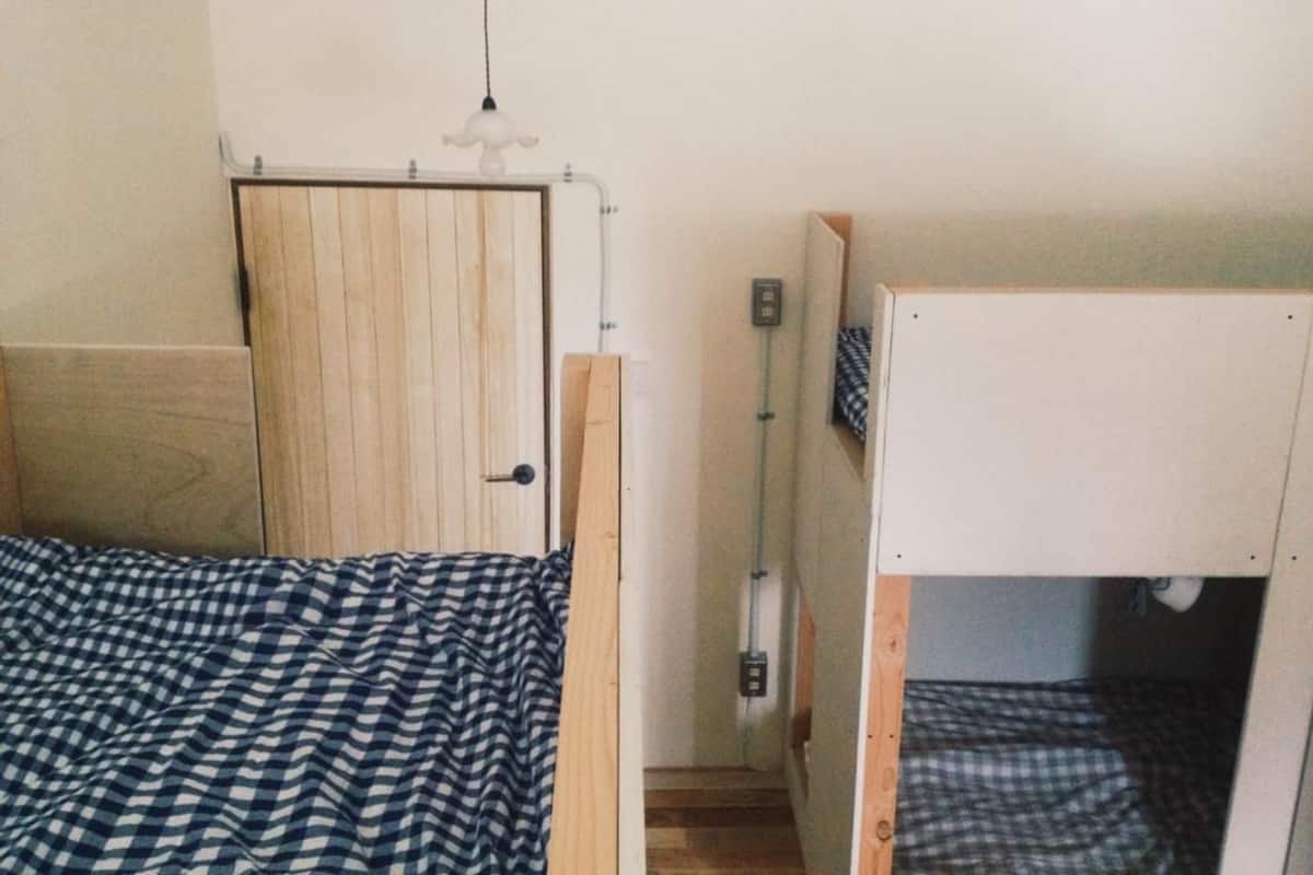 Una habitación pequeña y funcional con una cama individual, una puerta de madera y una cama litera.