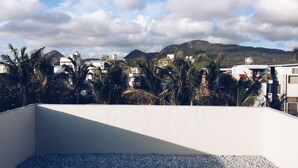A rooftop terrace with a view of a cityscape, palm trees, and mountains in the background. - Altrove House - Hostel (Hengchun)