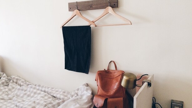 A bedroom with a bed, a hanging clothes rack, a brown leather bag, and a bedside table with a lamp and a power outlet. - Altrove House - Hostel (Hengchun)