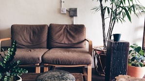 A cozy living room with a brown sofa, a wooden coffee table, a potted plant, and a rustic wooden stool. - Altrove House - Hostel (Hengchun)