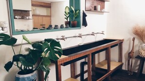A bathroom with a wooden vanity, a mirror, and a sink. There are plants on the vanity and a towel rack on the wall. - Altrove House - Hostel (Hengchun)