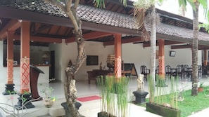 A traditional building with a tiled roof, wooden pillars, and a covered seating area with chairs and a table. - Hotel Melamun (Buleleng)