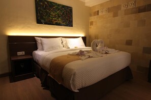 A hotel room with a large bed, a nightstand, a wall-mounted painting, and a patterned wall. - Hotel Melamun (Buleleng)