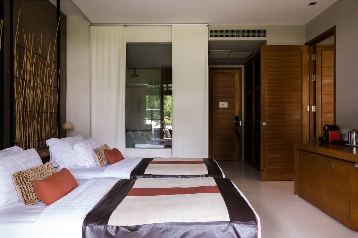 A hotel room with two beds, a wooden wardrobe, and a kitchenette.