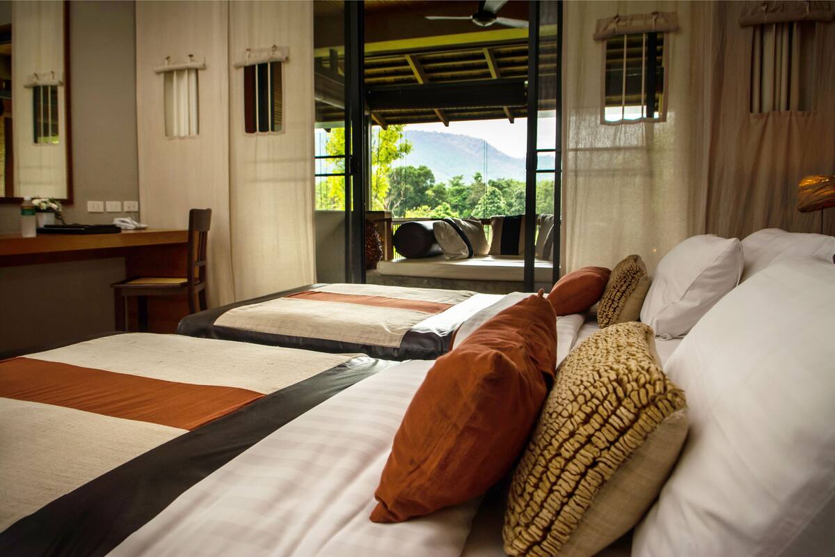A hotel room with two beds, a desk, and a view of the outdoors.