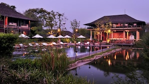 A resort with a pool, lounge chairs, umbrellas, and a building with a thatched roof. - Kirimaya Golf Resort Spa (Pak Chong)