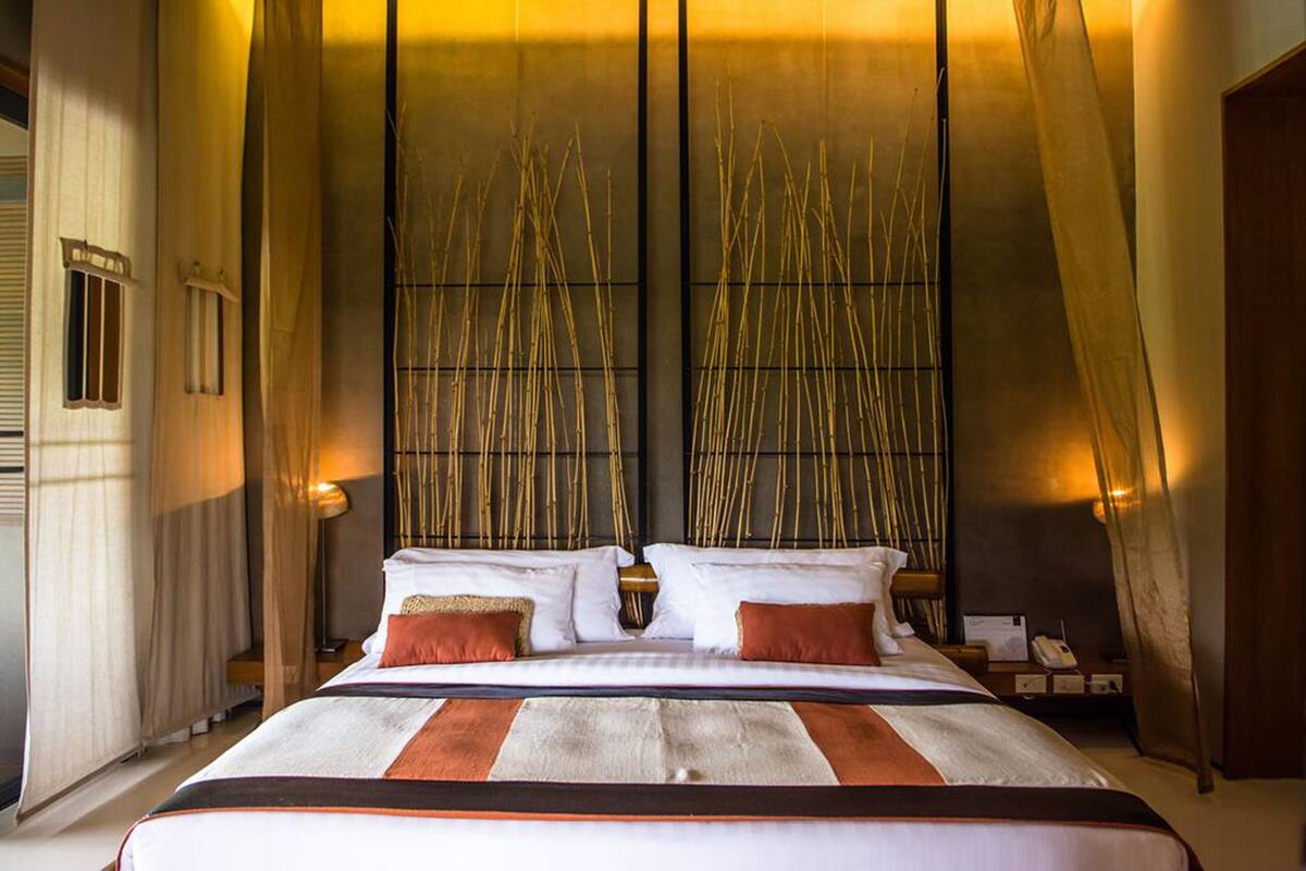 A large bed with a striped bedspread, two pillows, and a bedside table with a lamp.