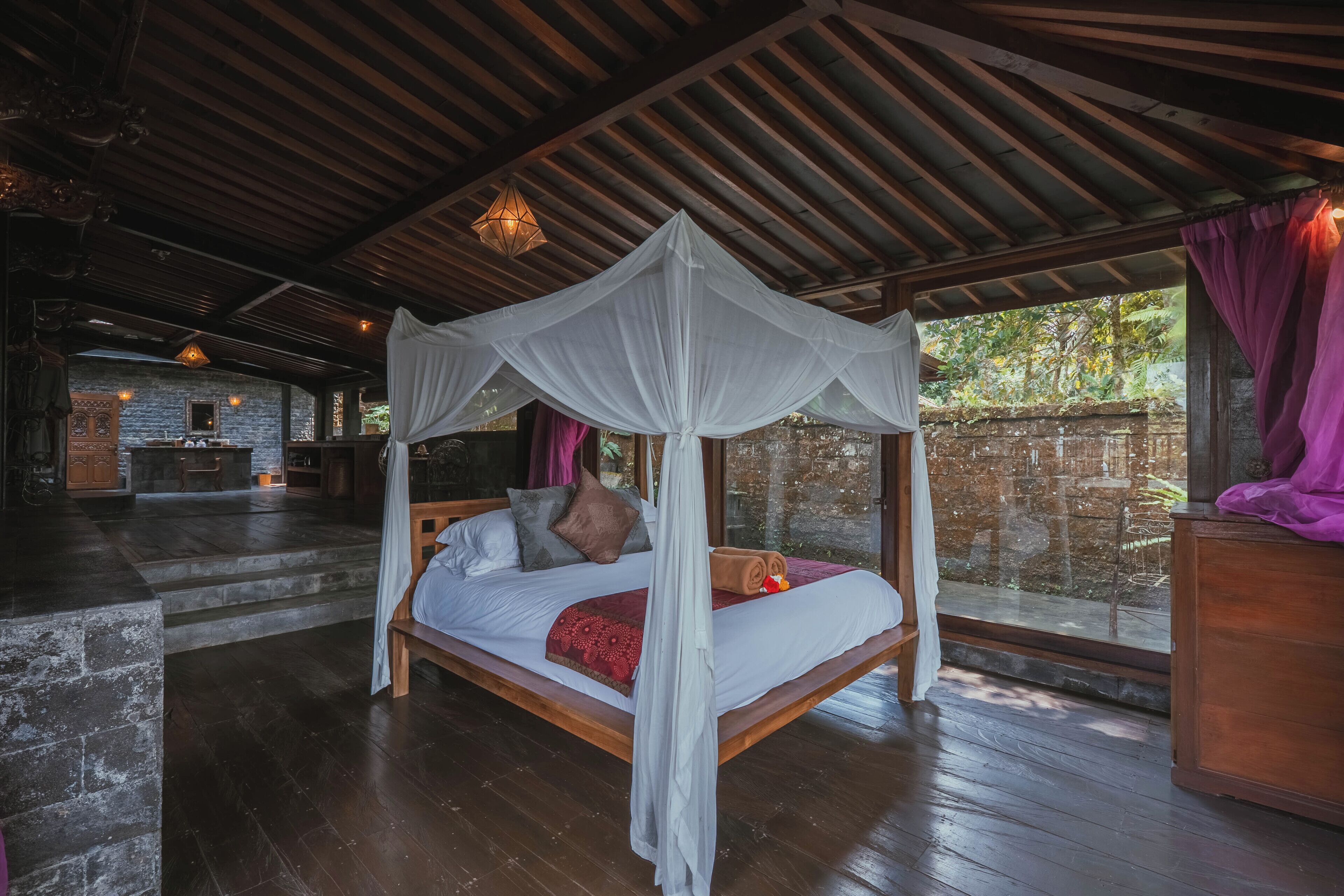 Un dormitorio con cama a dosel, suelo de madera, pared de piedra y vistas a la vegetación.