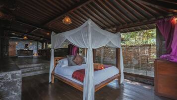 Un dormitorio con cama a dosel, suelo de madera, pared de piedra y vistas a la vegetación.