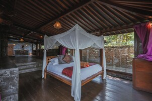 Un dormitorio con cama a dosel, suelo de madera, pared de piedra y vistas a la vegetación.