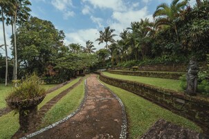 Un sendero atraviesa un jardín con palmeras y una estatua.