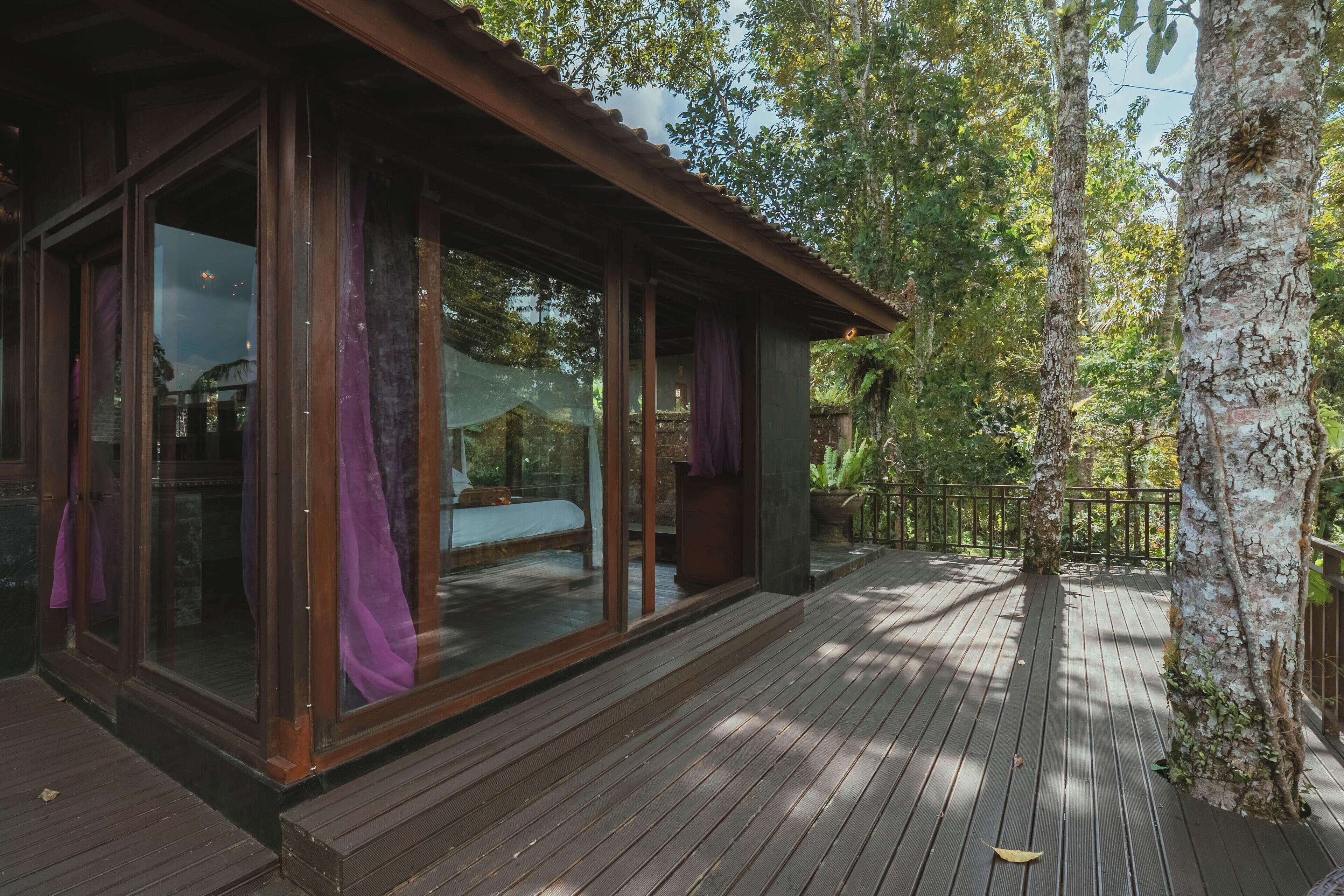 Un terrazzo in legno con pareti di vetro, un letto e vista sugli alberi circostanti.