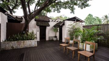 A wooden deck with chairs and potted plants, a stone wall, and a building with a tiled roof.
