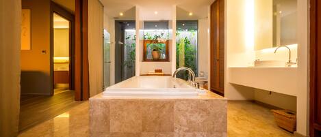 A modern bathroom with a large marble sink, a glass shower enclosure, and a wooden door.