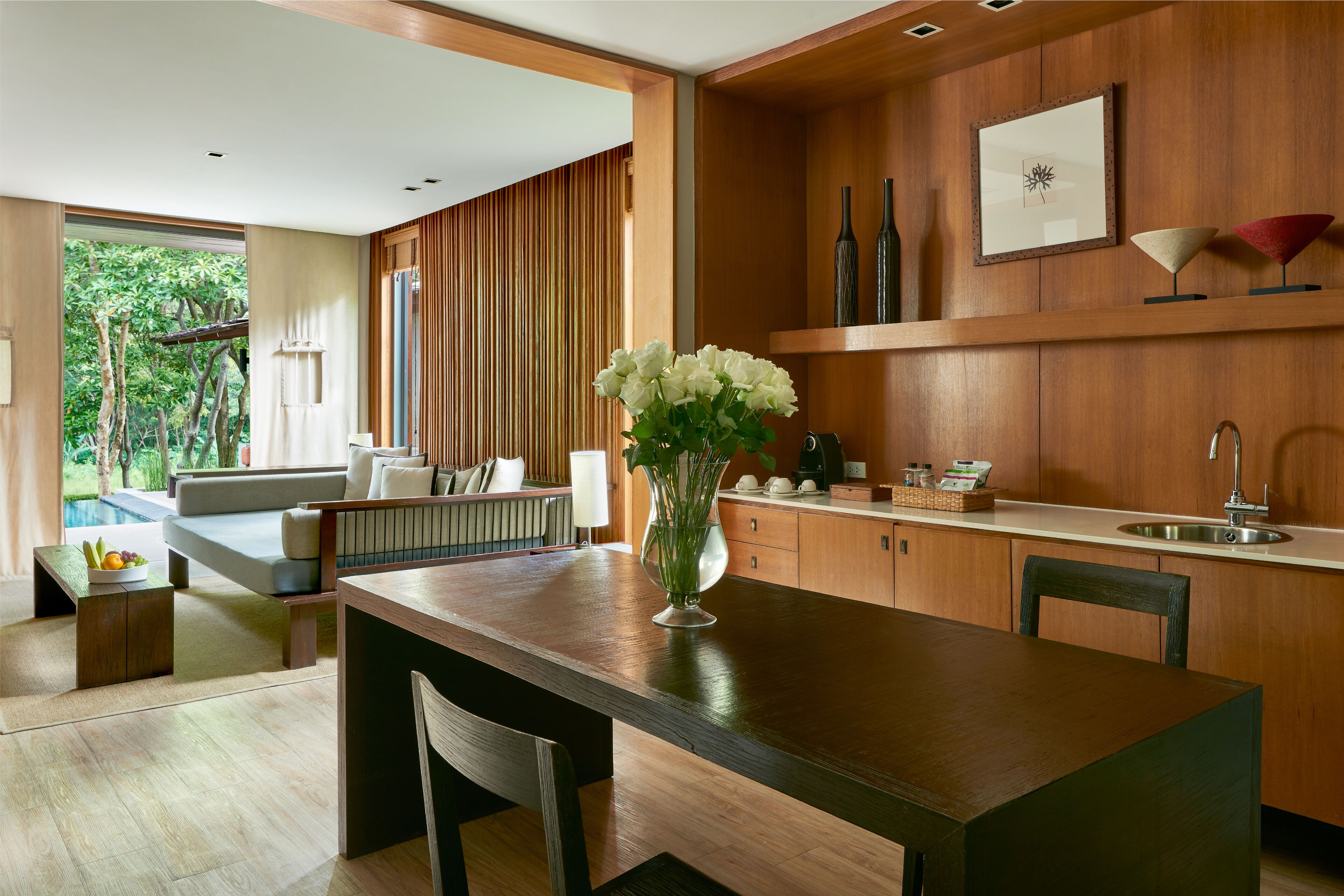 A modern kitchen with wooden cabinets, a dining table, and a vase of white flowers.