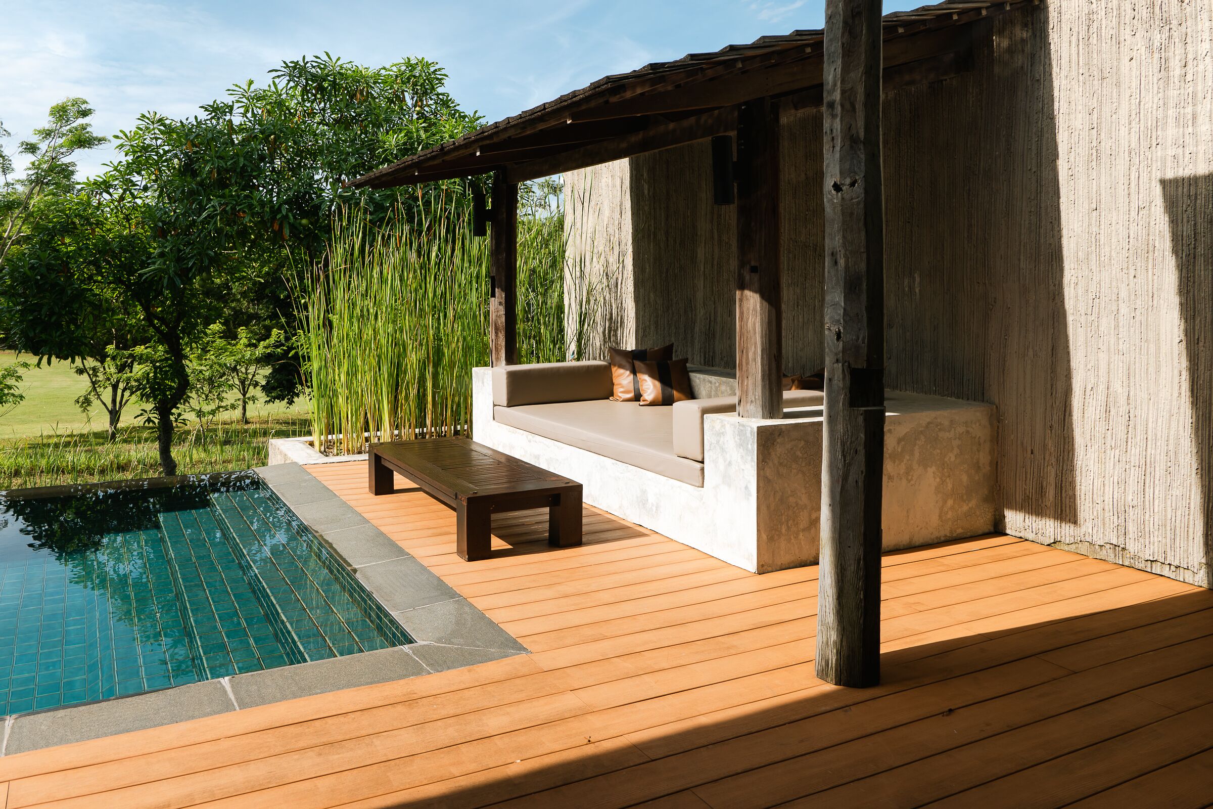 Eine Holzterrasse mit Pool, einer Sitzecke mit Kissen und einer Pergola.