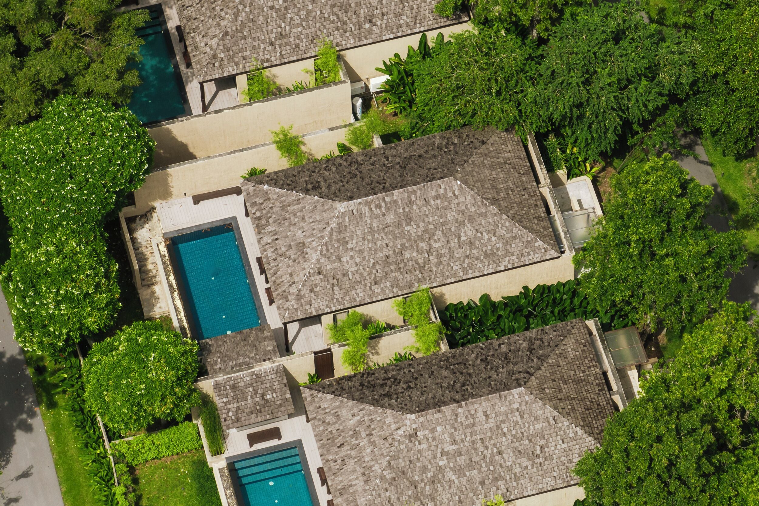 A resort with multiple swimming pools, lush greenery, and a tiled roof.