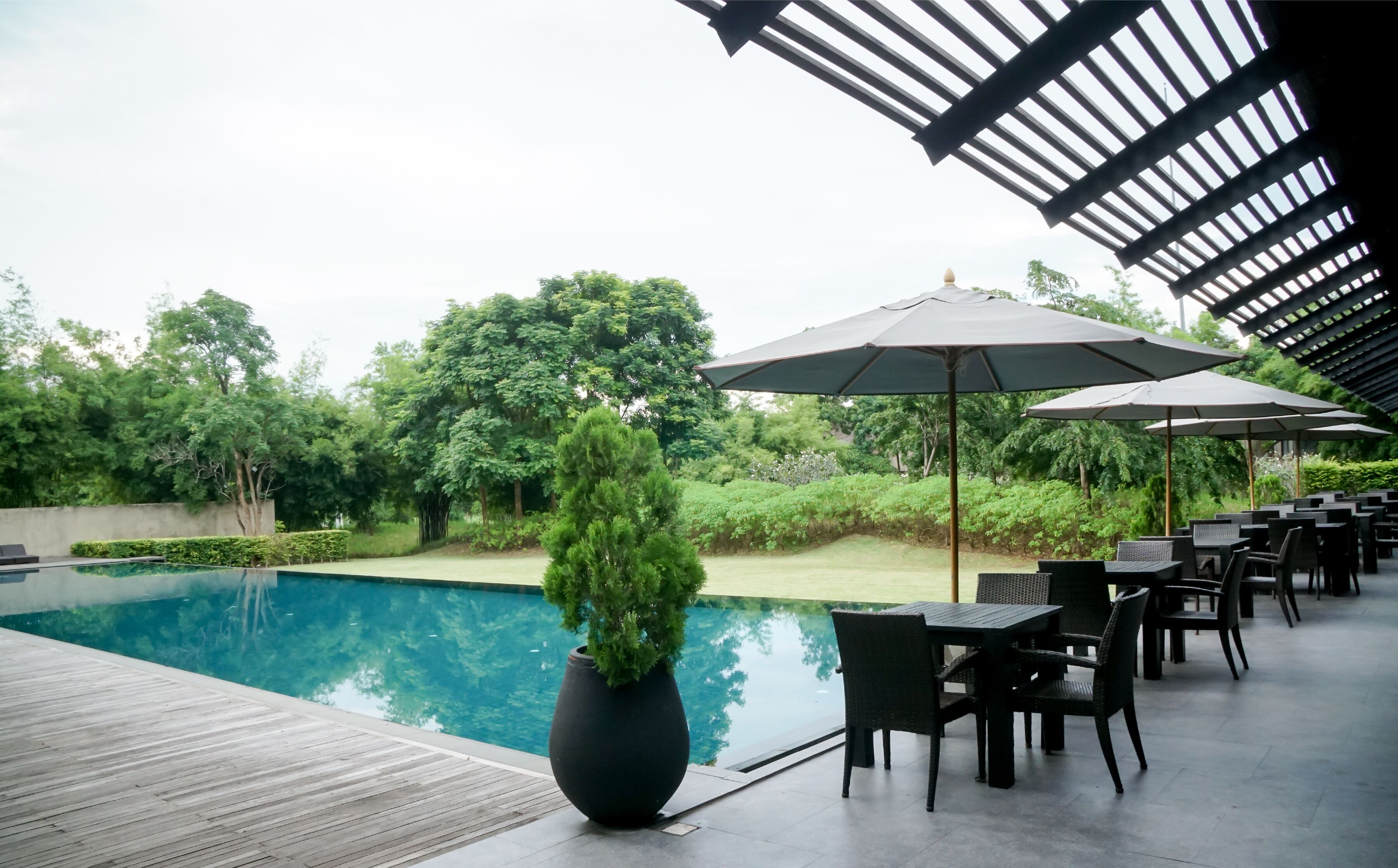 Un espace aménagé au bord de la piscine, avec une terrasse en bois, des sièges d’extérieur et des parasols.