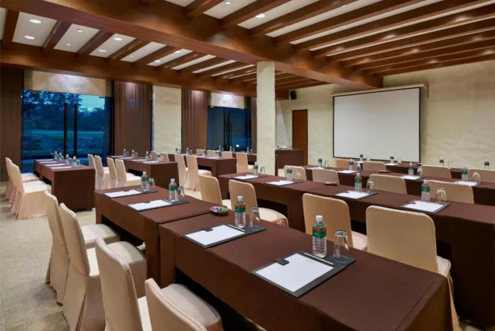 Un salón de conferencias con varias mesas, sillas y una pantalla de proyección.