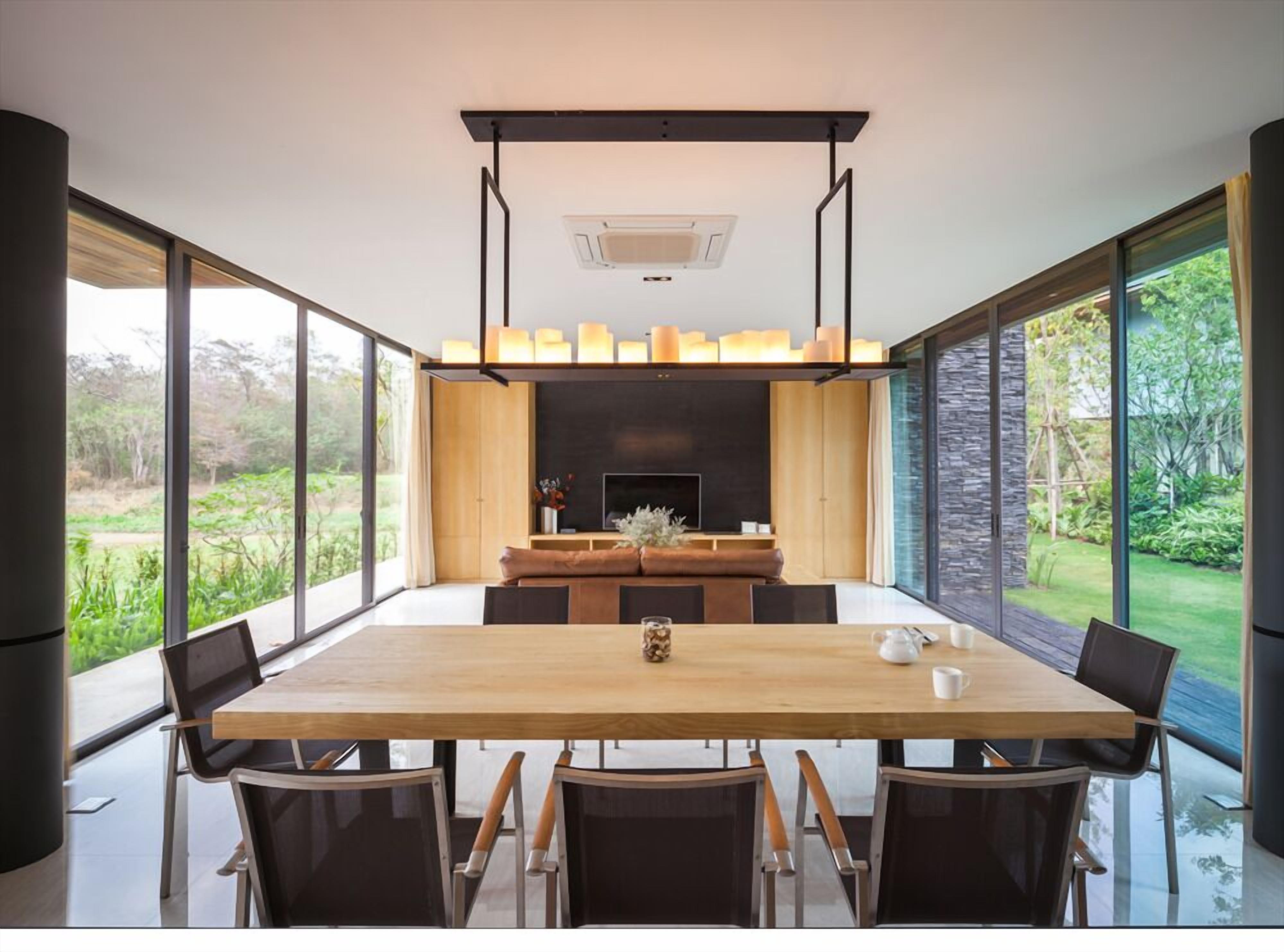 A modern dining area with a large table, chairs, a fireplace, and large windows offering a view of the outdoors.