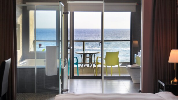 Habitación de hotel con balcón, vista al mar, cama, mesa y sillas.