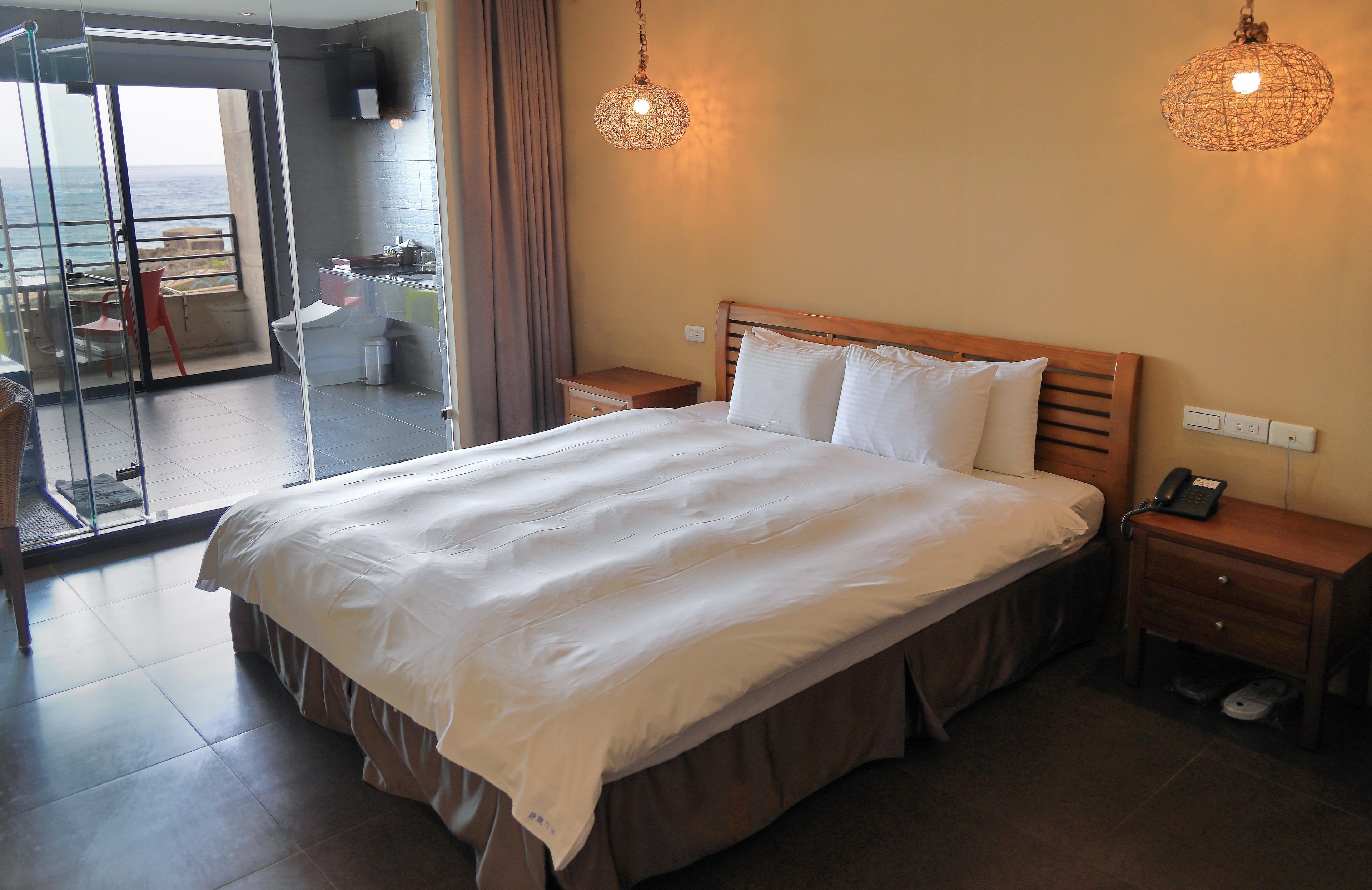 A hotel room with a large bed, bedside tables, a phone, and a view of the sea through a glass door.