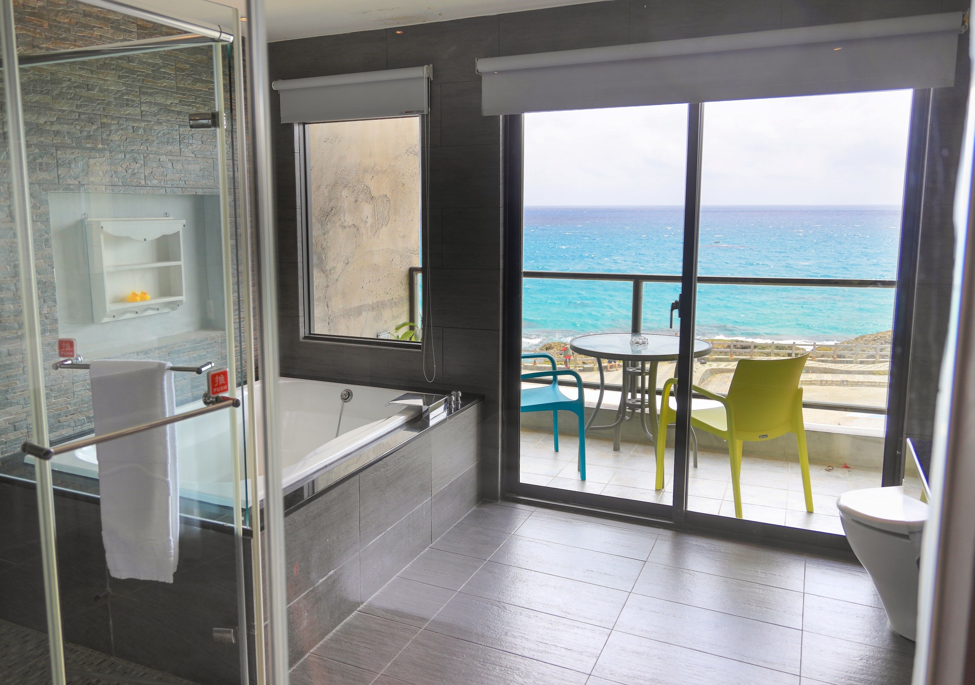 A bathroom with a bathtub, a glass shower enclosure, and a view of the ocean through large windows.