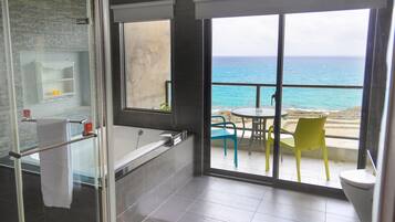 A bathroom with a bathtub, a glass shower enclosure, and a view of the ocean through large windows.