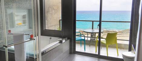 A bathroom with a bathtub, a glass shower enclosure, and a view of the ocean through large windows.