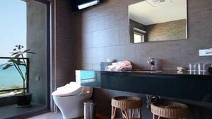Un baño moderno con un espejo grande, baldosas oscuras, un inodoro y dos taburetes.