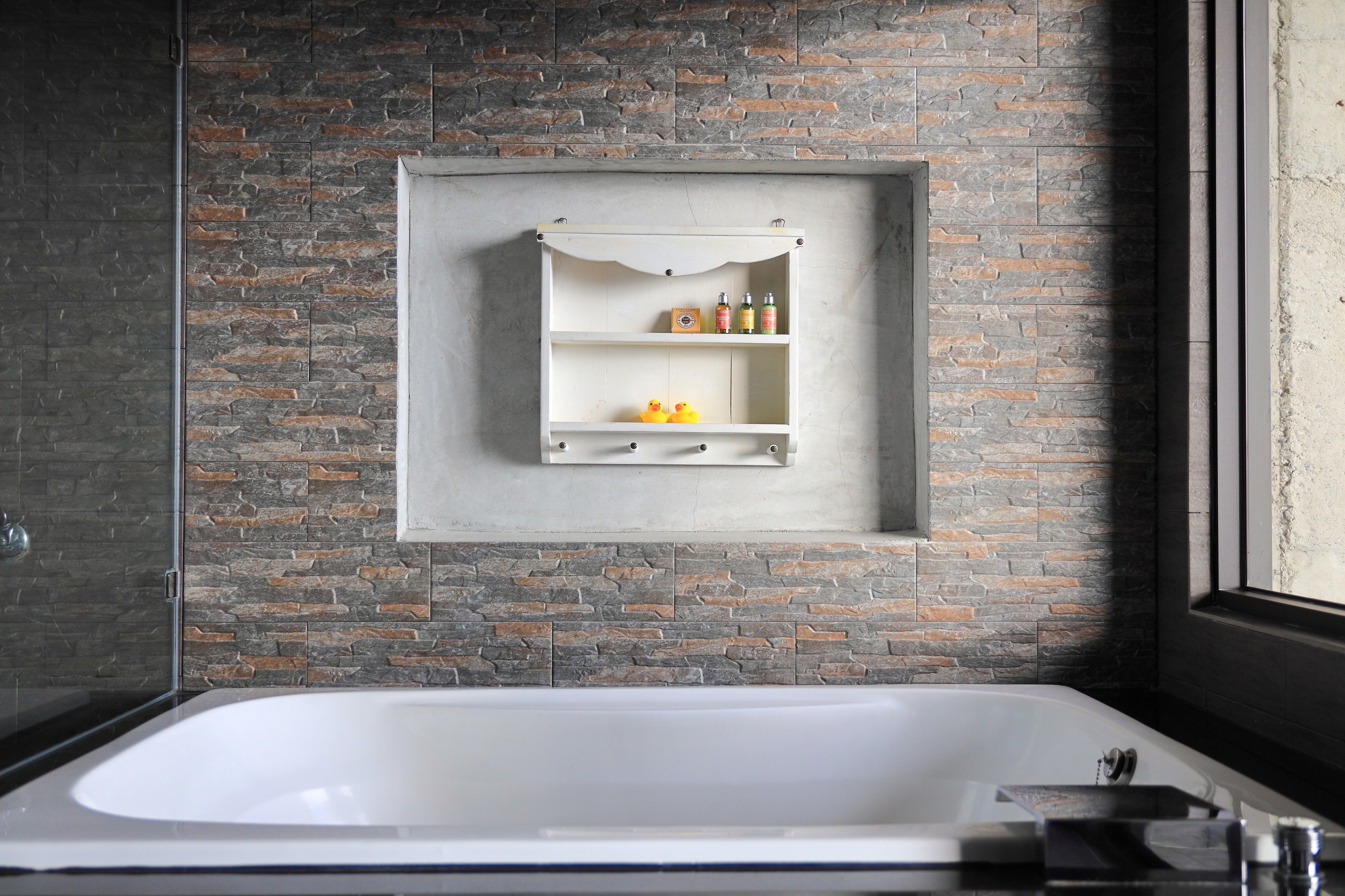 Ein modernes Badezimmer mit Steinwand, freistehender Badewanne und integriertem Ablagebereich für Pflegeprodukte.