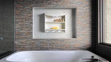 Ein modernes Badezimmer mit Steinwand, freistehender Badewanne und integriertem Ablagebereich für Pflegeprodukte.