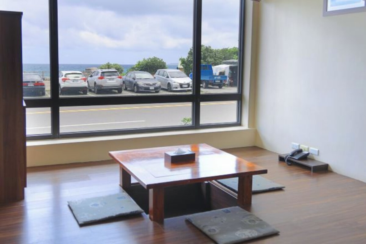 A room with a large window, a wooden table, and a view of a parking lot.