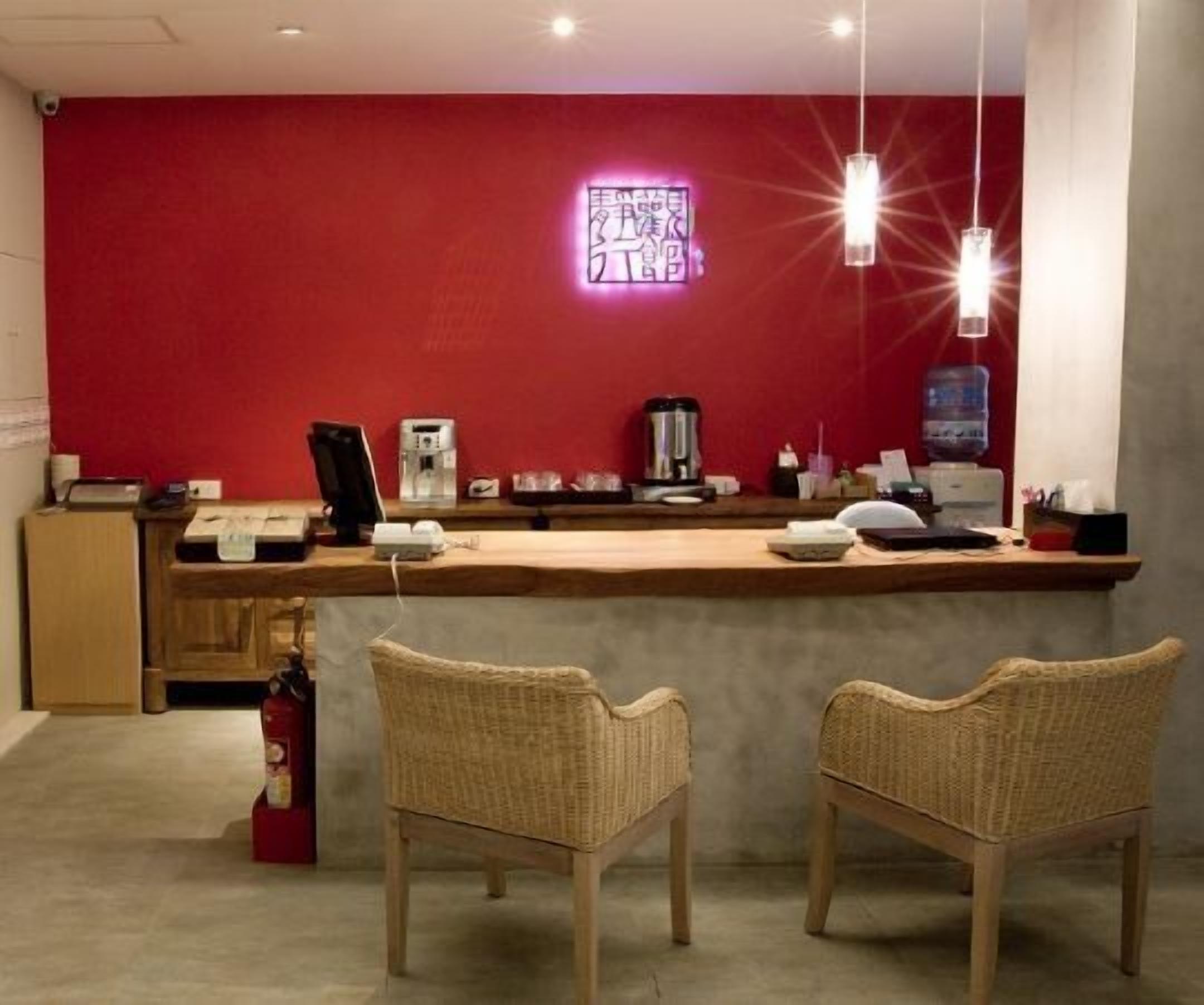 Ein Empfangsbereich mit roter Wand, einer Neonreklame, einer Holztresen und zwei Korbstühlen.