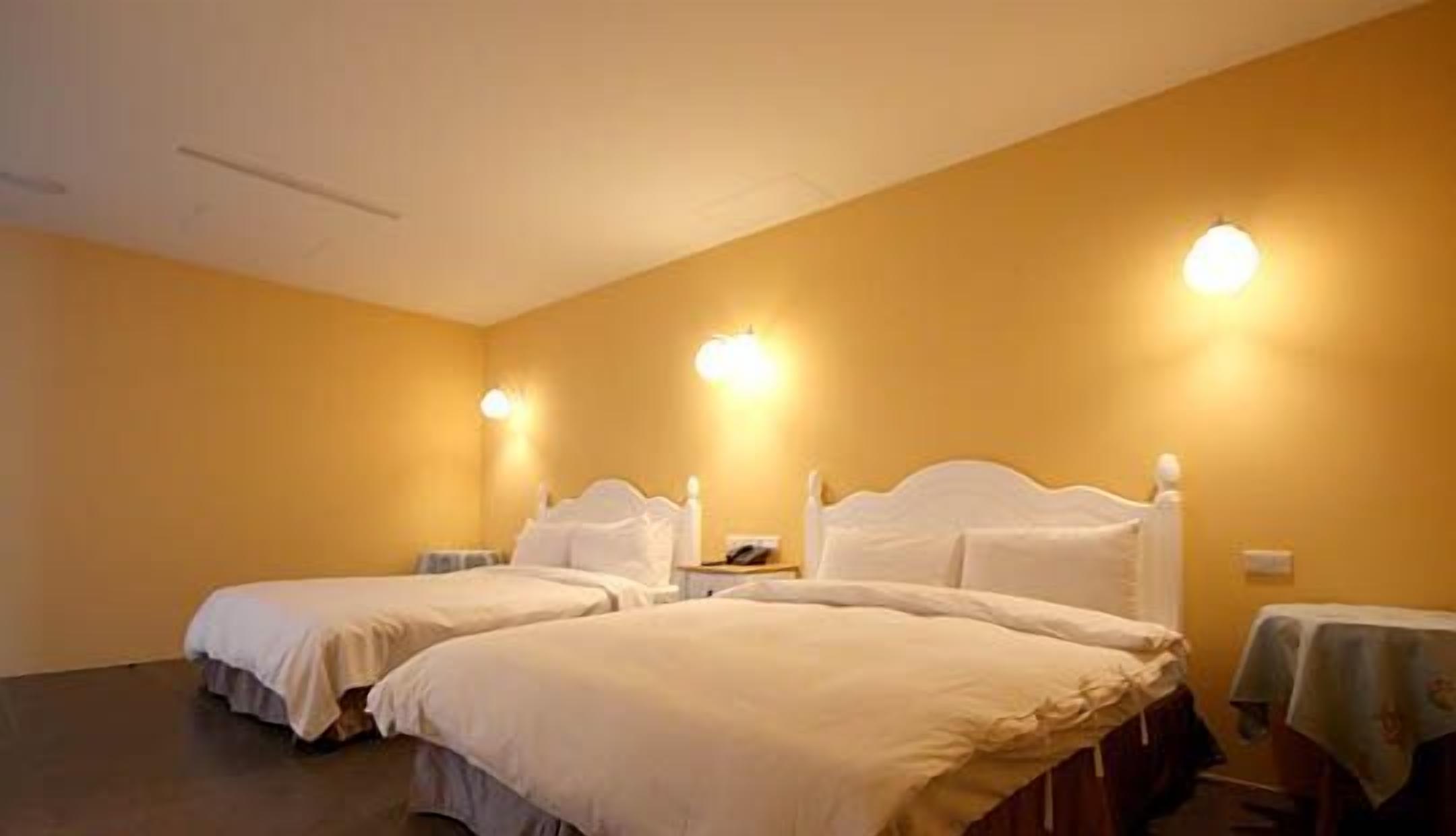 Une chambre d’hôtel avec deux lits, une table de chevet et des lampes fixées au mur.