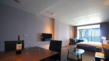 A hotel room with a bed, a desk, a chair, a small table, and a bottle of wine.