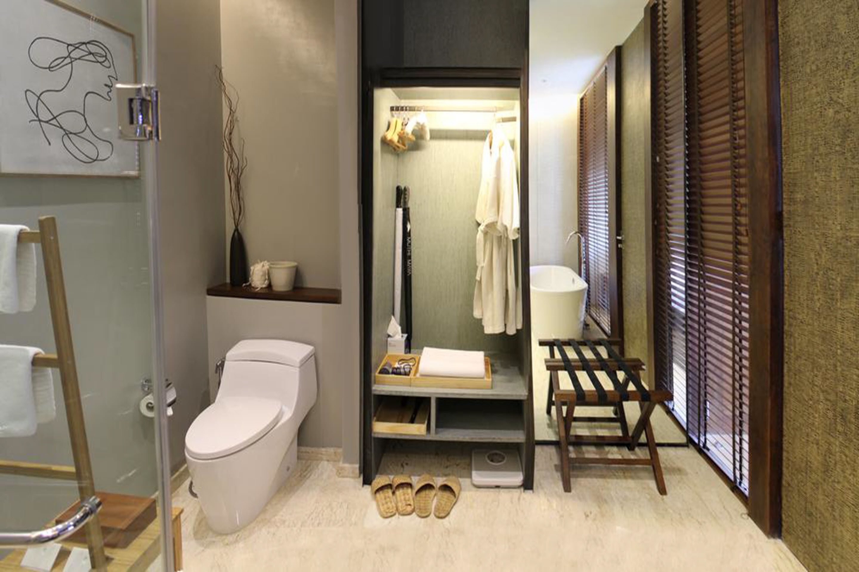 A compact bathroom with a toilet, a shelf with towels, a small bench, and a scale.