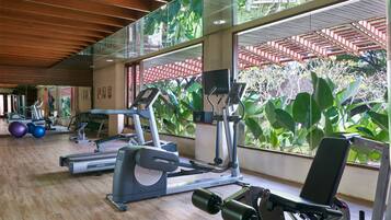 A gym with exercise equipment, large windows, and a view of greenery.