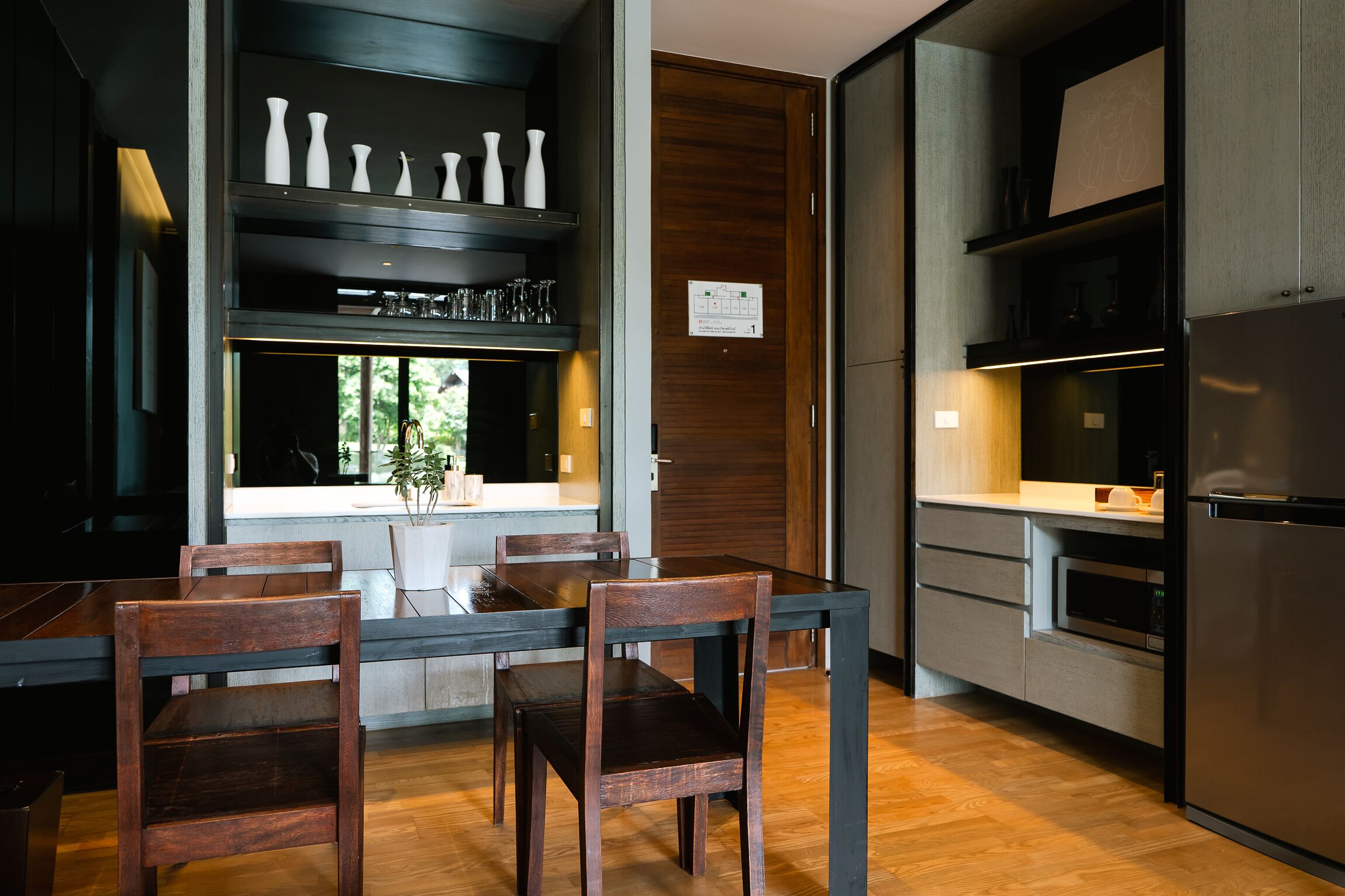A modern kitchen with a dining area, wooden chairs, a built-in oven, and a refrigerator.