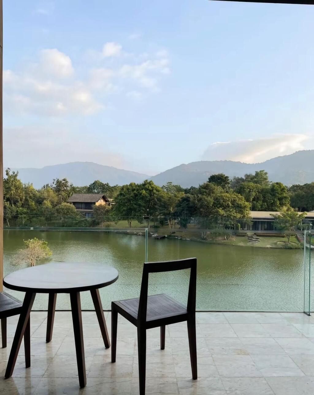 A terrace with a table and chairs overlooking a lake, with buildings and trees in the background.