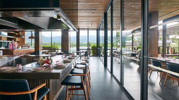 A modern restaurant with a long bar, high ceilings, and large windows offering a mountain view. - atta Lakeside Resort Suite (Pak Chong)