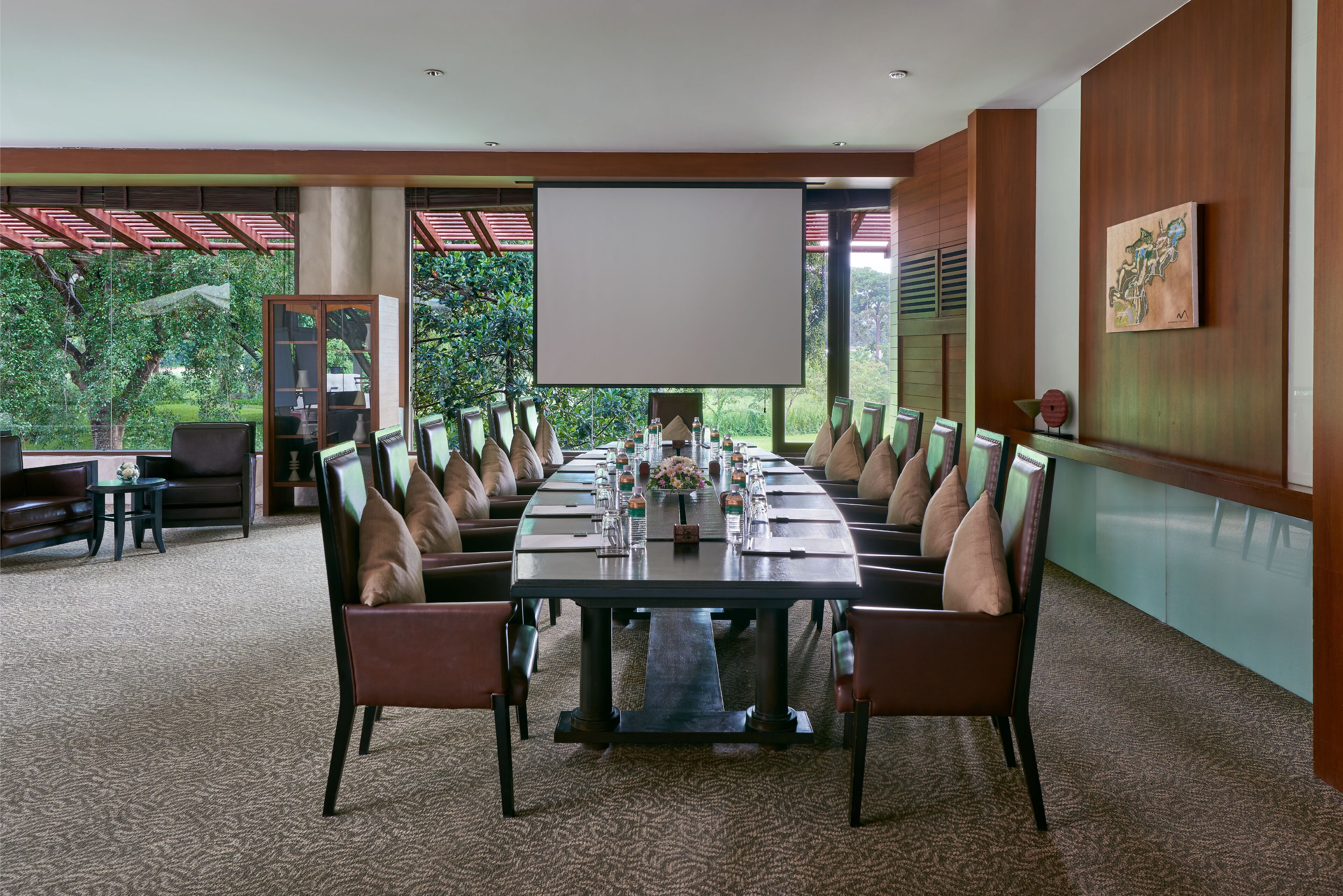 Een vergaderzaal met een lange tafel, stoelen, een scherm voor een projecteerder en uitzicht op groen buiten.