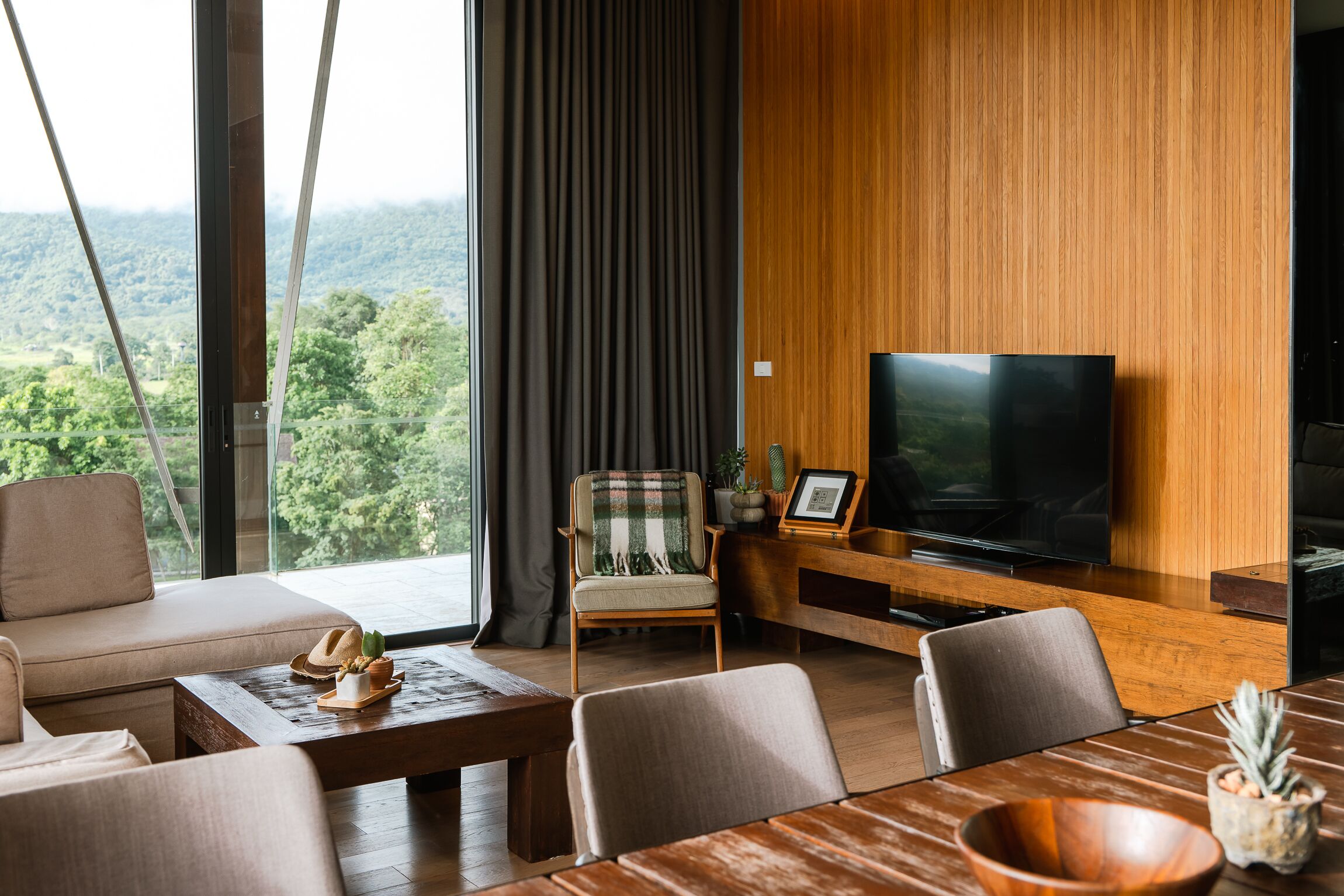 A modern living room with a large TV, wooden panel walls, a sofa, and a dining table.